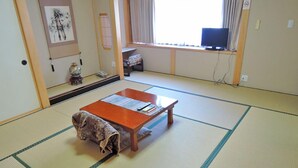 A traditional Japanese room with tatami flooring, a low wooden table, and a futon bed. - Yayoi Ryokan (Ono)