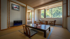 Ein traditioneller japanischer Raum mit Tatami-Böden, einem niedrigen Tisch mit Teeausrüstung und einem Fernseher.