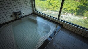 Ein Badezimmer mit einer großen Badewanne, gefliesten Wänden und einem Fenster mit Blick auf einen Fluss.