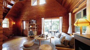 A cozy log cabin interior with a wooden staircase, a dining area, a sofa set, and a kitchen area. - Etowa Kasama (Kasama)
