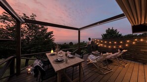 Une terrasse extérieure avec une table dressée pour les repas, des chaises et des guirlandes lumineuses.
