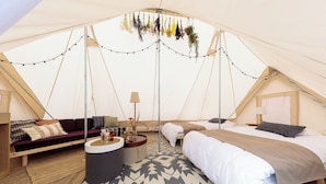 A tented accommodation with a bed, sofa, and round table, featuring a patterned rug and hanging plants. - Etowa Kasama (Kasama)
