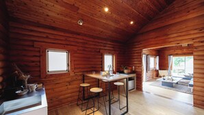 A wooden cabin interior with a kitchen area, bar stools, and a dining table. - Etowa Kasama (Kasama)