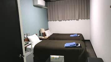 A hotel room with two beds, a desk, a chair, a TV, and an air conditioning unit.