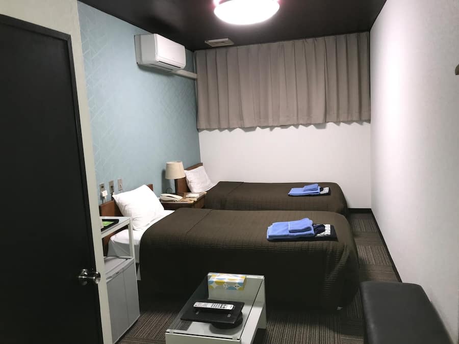 Een hotelkamer met twee bedden, een bureau, een stoel, een televisie en een airconditioning.
