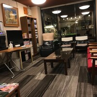A hotel lobby with a reception desk, a bookshelf, leather chairs, a glass coffee table, and a large window with a view of the street.