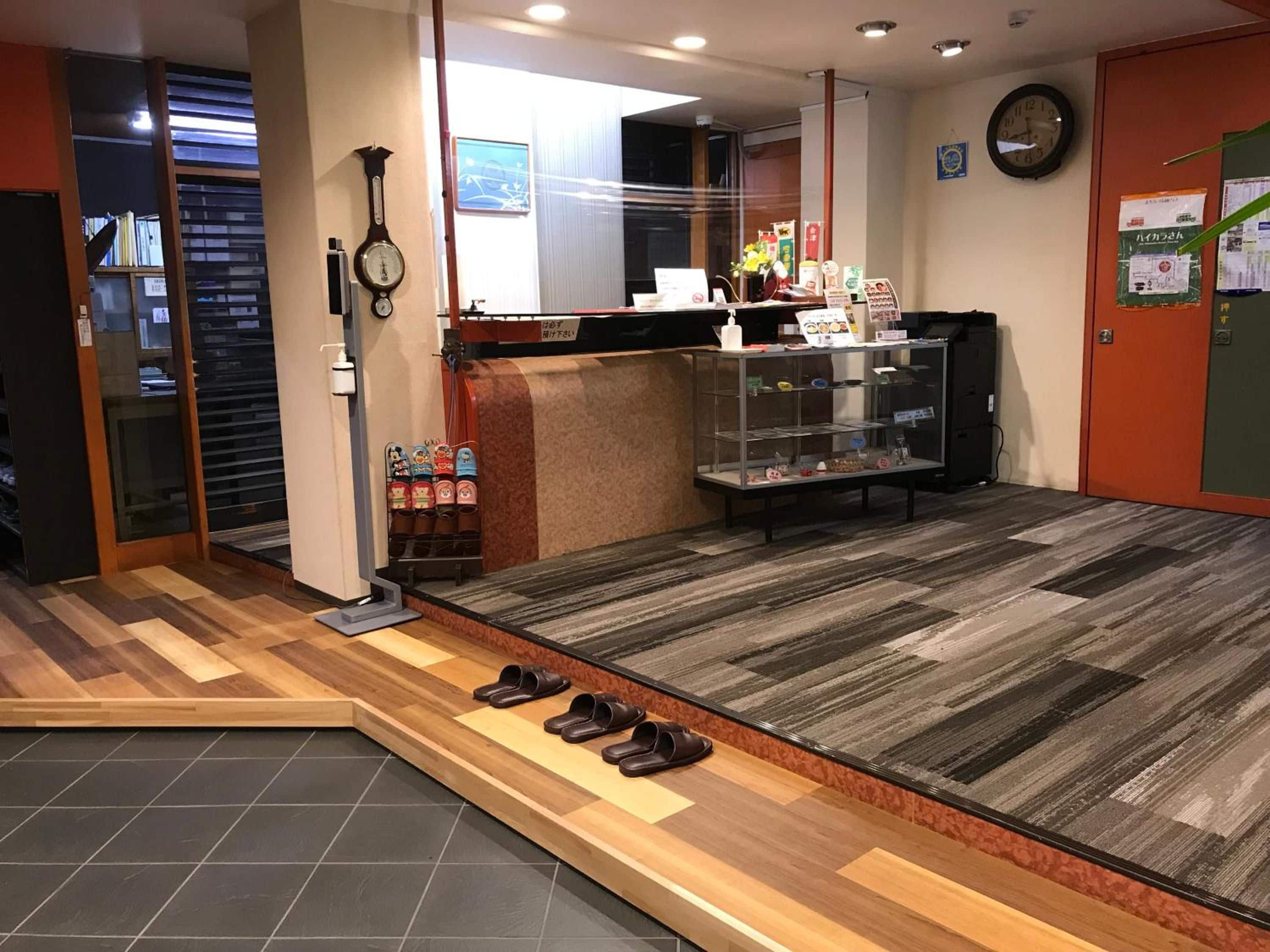 A reception area with a wooden floor, a reception desk, a clock, and a shoe rack.