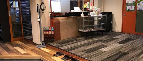 A reception area with a wooden floor, a reception desk, a clock, and a shoe rack.