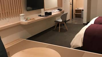 Una habitació d'hotel amb llit, escriptori, cadira, televisió i taula petita.