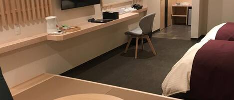 A hotel room with a bed, a desk, a chair, a TV, and a small table.