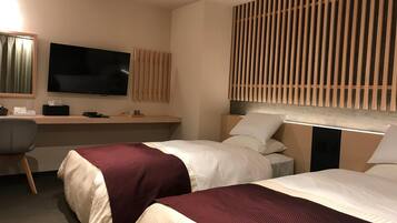 A hotel room with two beds, a desk, a television, and a wall-mounted panel.