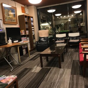 A hotel lobby with a reception desk, a bookshelf, leather chairs, a glass coffee table, and a large window with a view of the street. - Aizu Tsuruya Hotel (Aizuwakamatsu)