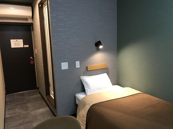 A hotel room with a bed, a bedside table, a wall-mounted light, and a door with a sign. - Aizu Tsuruya Hotel (Aizuwakamatsu)