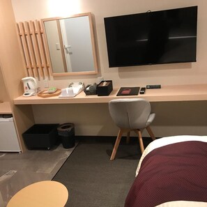 A hotel room with a desk, a television, a chair, a bed, and a small trash bin.