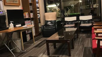 A hotel room with a large window, a desk with a computer, a bookshelf, and a seating area with chairs.