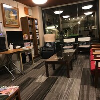 Habitación de hotel con un ventanal grande, un escritorio con computadora, una estantería y un rincón de descanso con sillas.