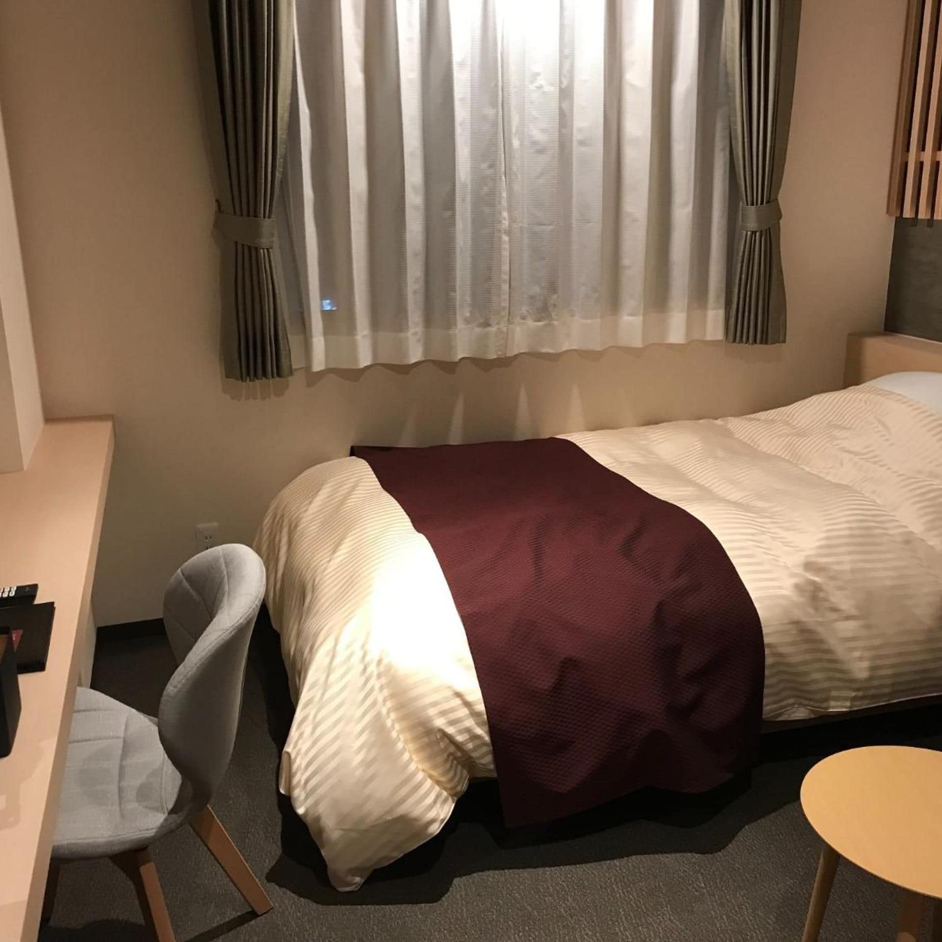 Quarto de hotel com cama, escrivaninha, cadeira e mesa pequena.