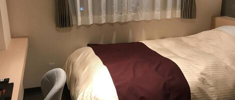 Quarto de hotel com cama, escrivaninha, cadeira e mesa pequena.