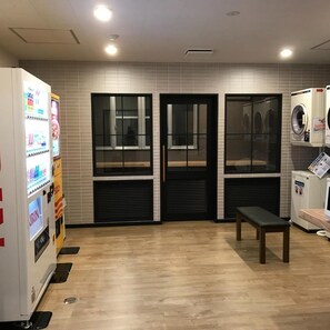 A laundry facility with a vending machine, a bench, and a washing machine. - Aizu Tsuruya Hotel (Aizuwakamatsu)