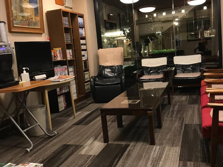 A hotel lobby with a reception desk, a bookshelf, leather chairs, a glass coffee table, and a large window with a view of the street.