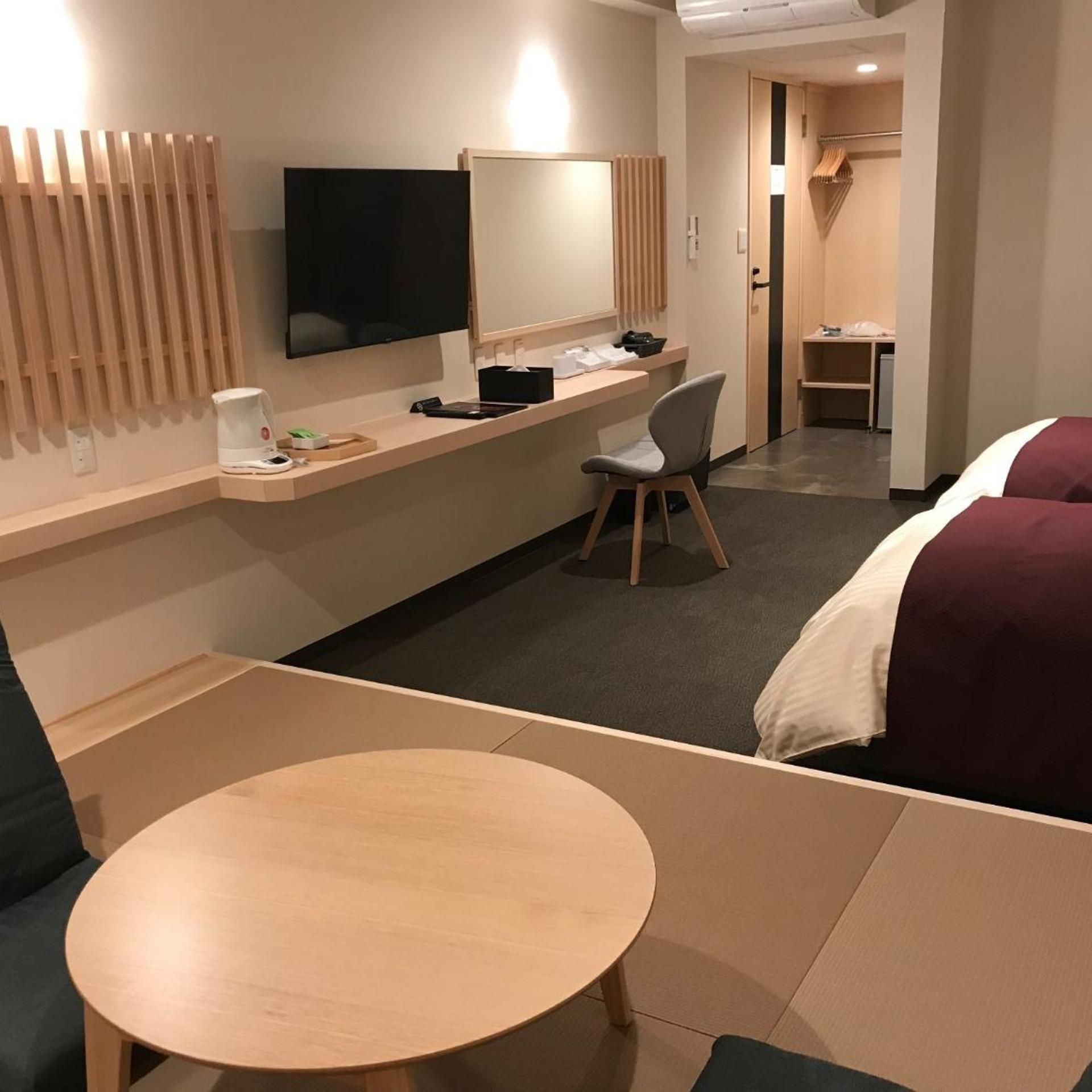 A hotel room with a bed, a desk, a chair, a TV, and a small table.