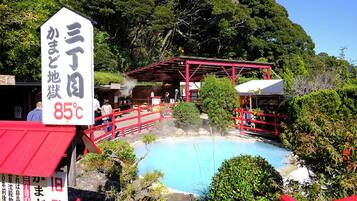 A hot spring area with a red-roofed building, a sign indicating the temperature, and a natural landscape with trees.