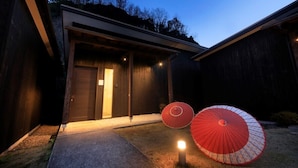 A modern house with a garage door, two red umbrellas, and a well-lit entrance. - Beppu Onsen Wanko no Yado Yururi (Beppu)