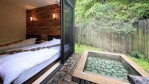 A bedroom with a large bed, a wooden headboard, and a glass door leading to a stone hot tub. - Beppu Onsen Wanko no Yado Yururi (Beppu)