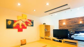 A modern living room with a wooden table, a sofa, a TV, and a bookshelf. - Beppu Onsen Wanko no Yado Yururi (Beppu)
