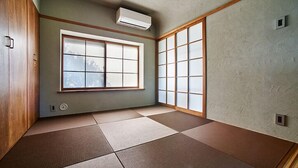 Een kamer met tatami vloerbedekking, een groot shoji-schermraam en een aan het plafond bevestigde airconditioner.