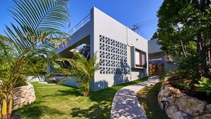 Een modern huis met een witte gevel, een decoratief rasterraam en een verzorgde tuin met palmboompjes en een pad van stenen.