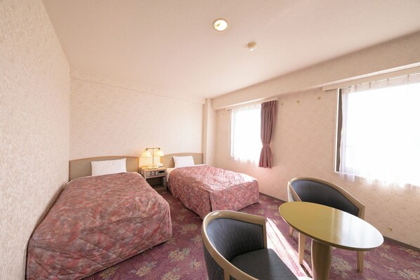 A hotel room with two beds, a small table, and a chair. - Main Hotel (Miyakonojo)