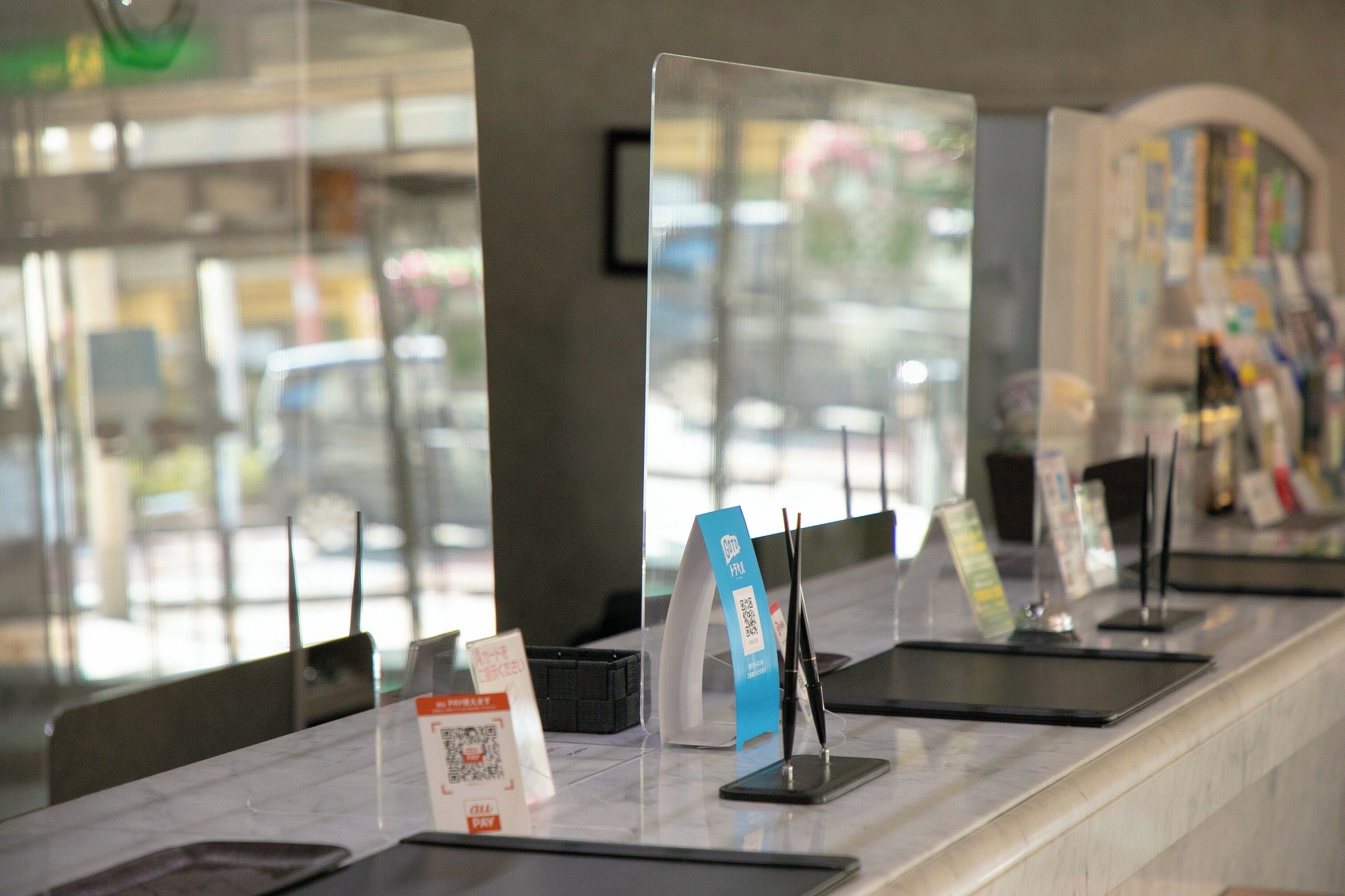 A reception desk with a glass partition, a digital screen, and a QR code for check-in.