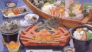 A seafood feast with a variety of dishes including a large crab, shrimp, and other seafood, served on a wooden table with a blue background. - Umi no Yado Sahei (Minamiechizen)