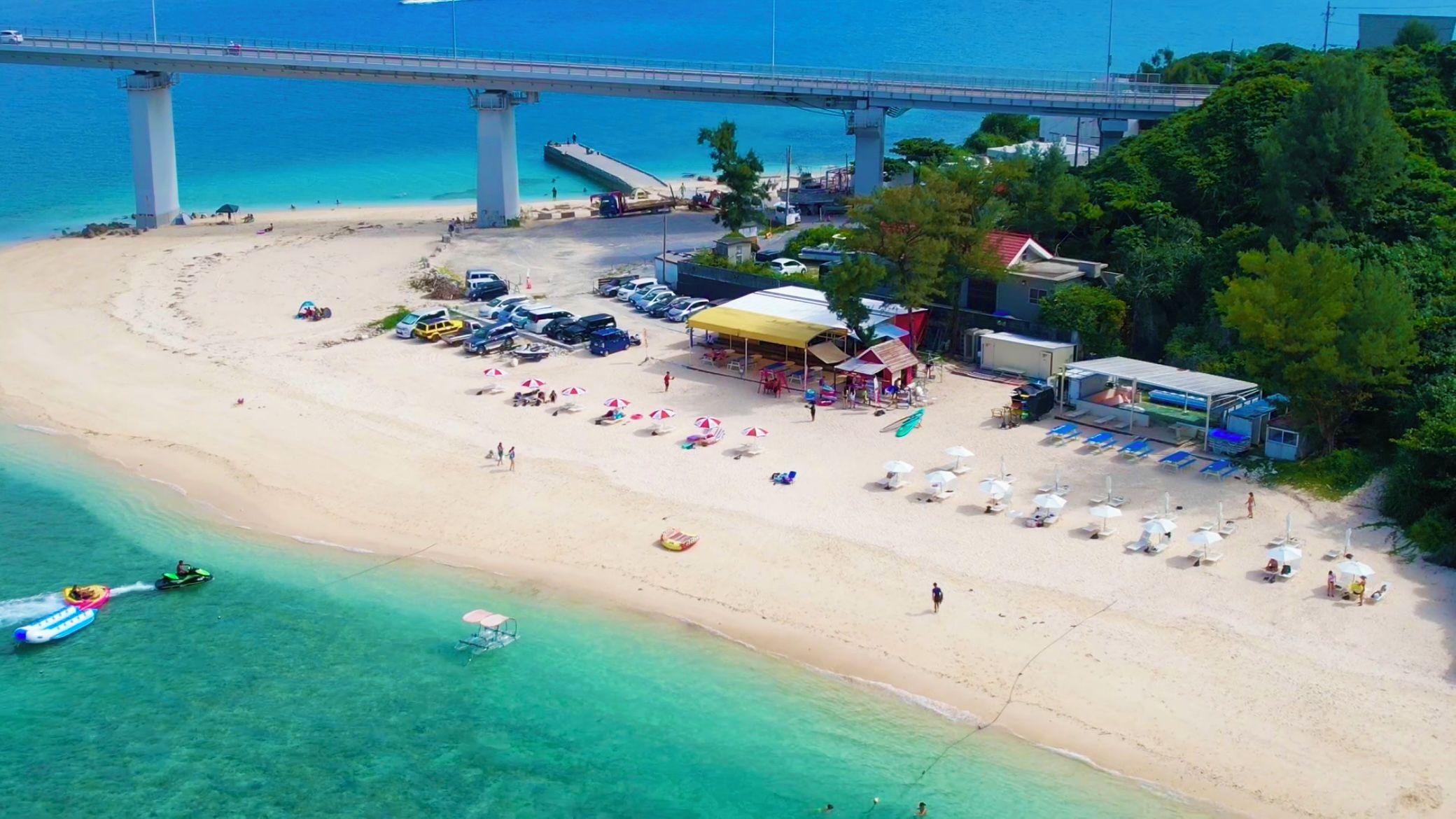 A beach with a pier, beach umbrellas, and a small building.