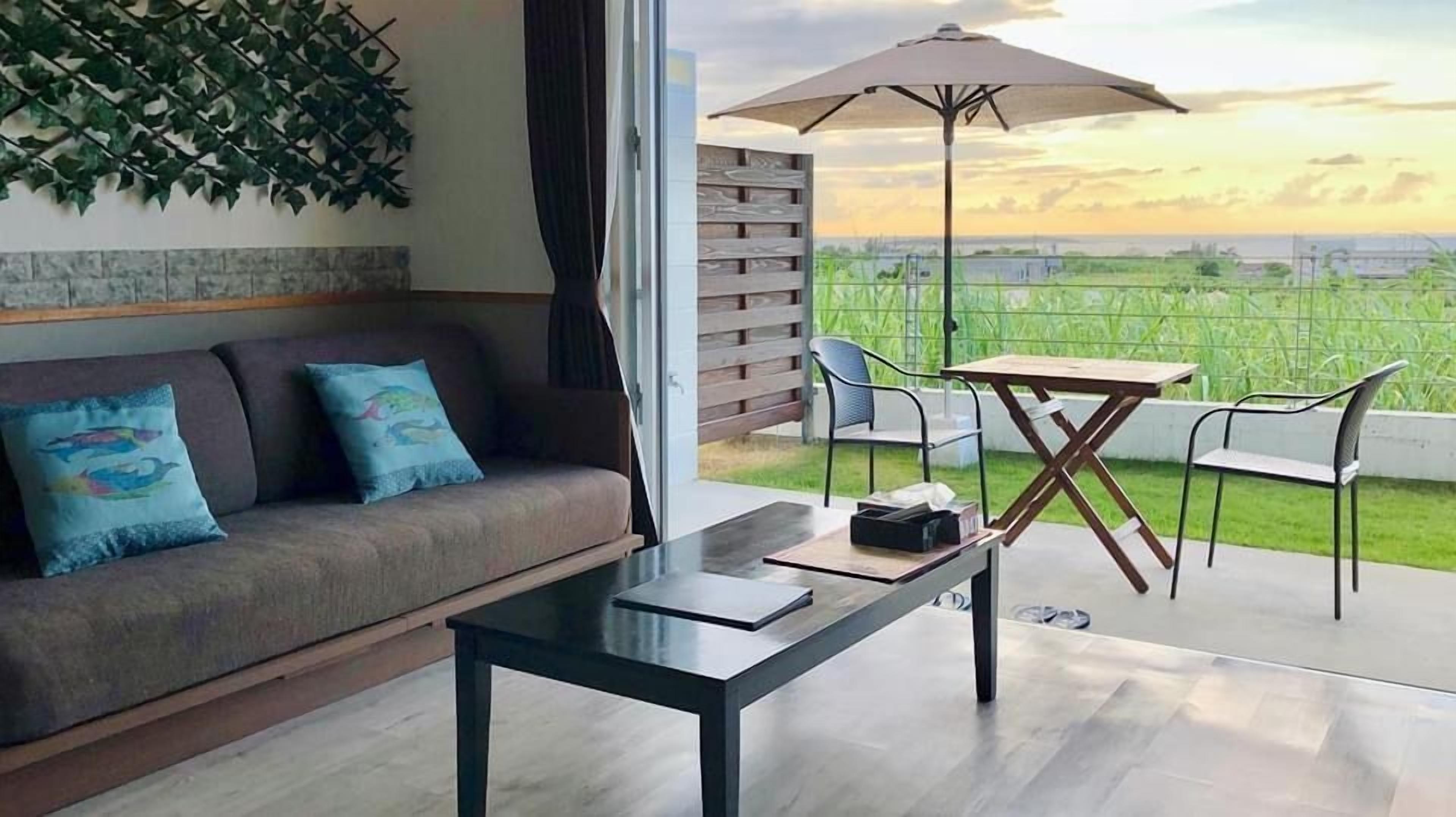A modern living room with a sofa, a coffee table, and a dining area with chairs and an umbrella.
