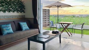 A modern living room with a sofa, a coffee table, and a dining area with chairs and an umbrella. - Island Hills Sesoko (Motobu)