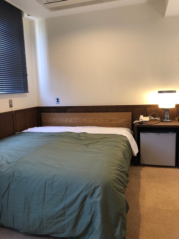A hotel room with a bed, a nightstand, a lamp, and a mini-fridge. - The Hotel Teramoto (Tanabe)
