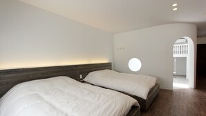 Et moderne soveværelse med to senge, en rund lampe og en træsenggavl.