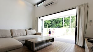 En moderne stue med sofa, sofabord og en skydedør til et udendørs område.
