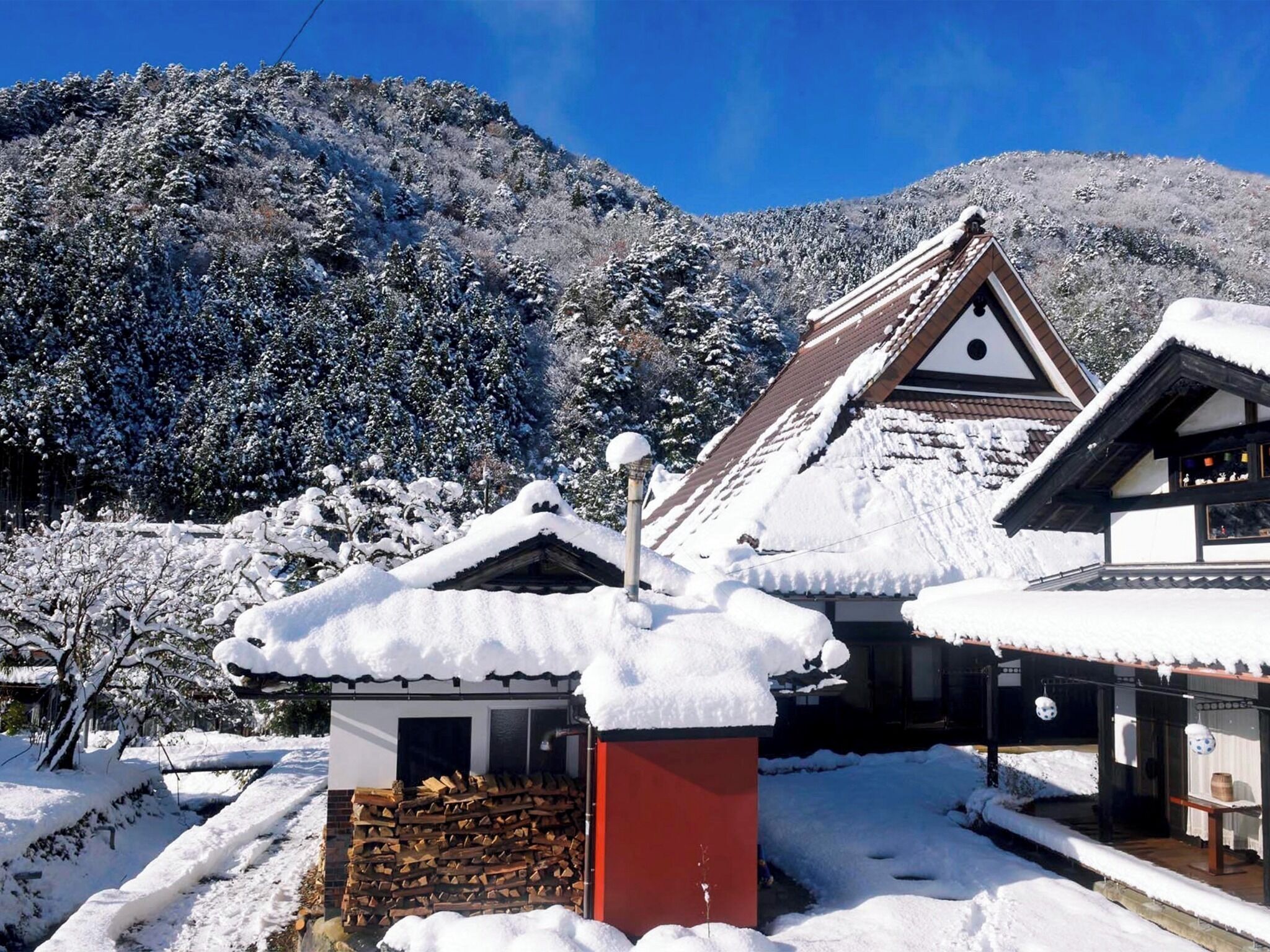 Um edifício tradicional em estilo japonês com telhado coberto de neve, emoldurado por uma paisagem montanhosa.