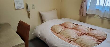 A hotel room with a bed, a desk, a chair, a wall-mounted phone, and a window with curtains.