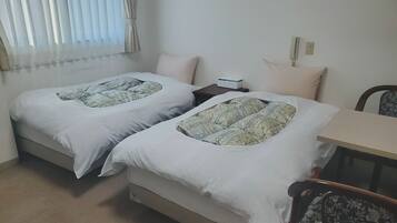 A twin room with two beds, a small table, a chair, and a window with curtains.