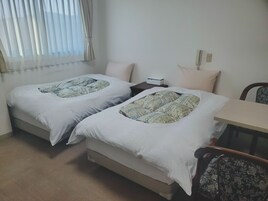 Habitación doble con dos camas, una mesita, una silla y un ventanal con cortinas.