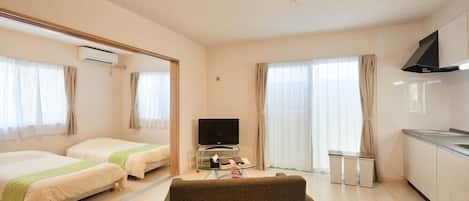 A hotel room with two beds, a television, a sofa, a kitchen area, and a large mirror.