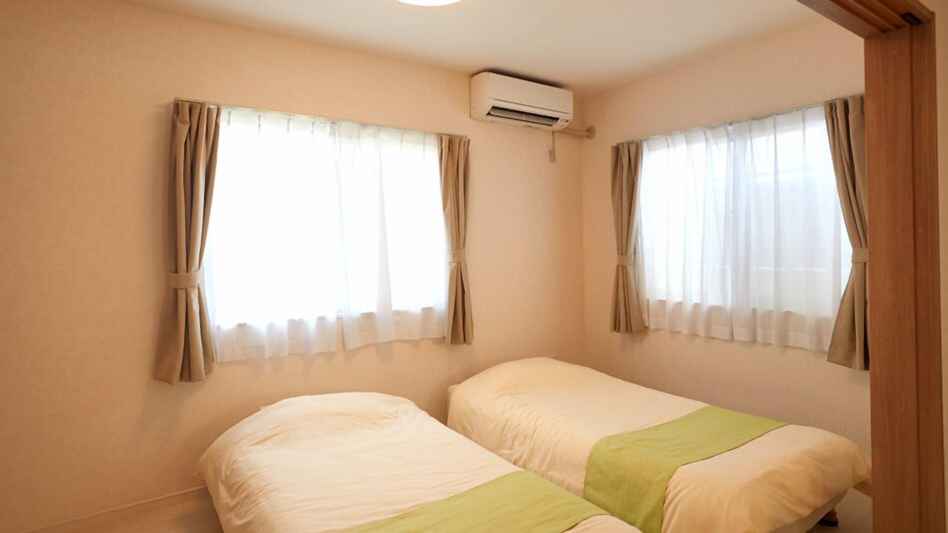 A room with two beds, beige walls, and an air conditioning unit.