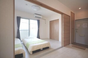 A bedroom with two beds, a window with curtains, an air conditioning unit, a wooden wardrobe, and a door. - Rainbow Terrace (Ginowan)