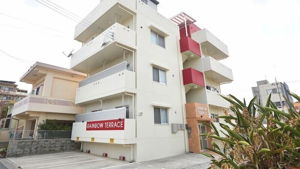 A multi-story building with balconies, a sign reading 'RAINBOW TERRACE,' and a visible entrance. - Rainbow Terrace (Ginowan)