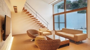 Ein modernes Wohnzimmer mit Treppe, großen Fenstern und einem Flachbildfernseher.