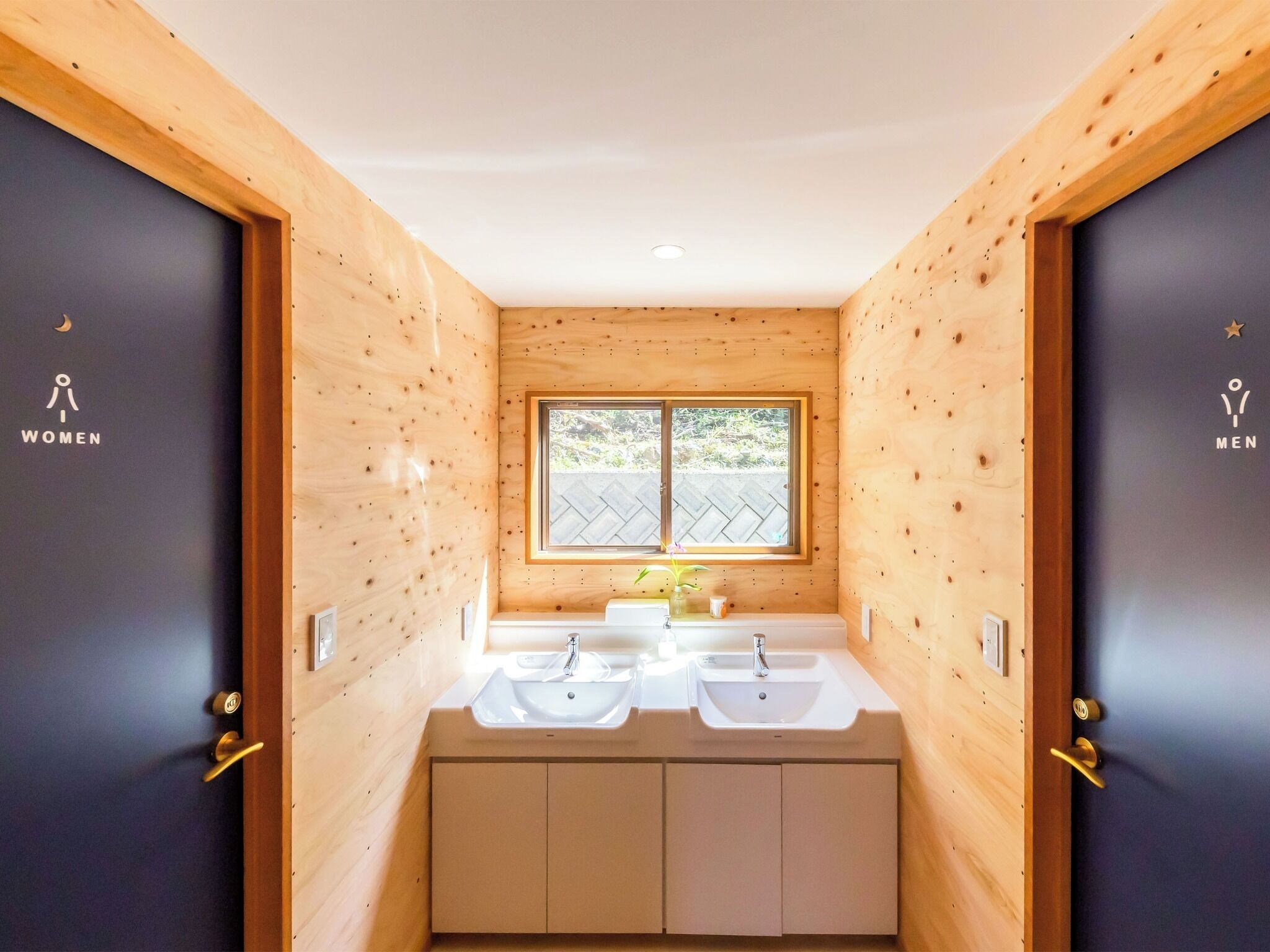 Un baño pequeño y con acabados de madera, con dos lavamanos y una ventana.